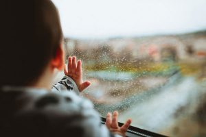 Kid touching and looking out a rainy window