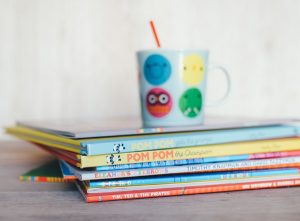 A stack of childrens' books and a colourful cup