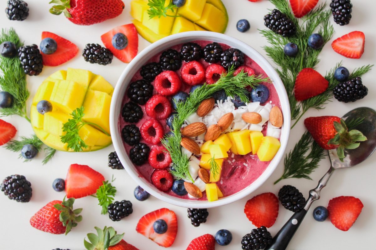 A yoghurt bowl with raspberries, blackberries, mangoes, coconut, blueberries and almonds surrounded by fruit