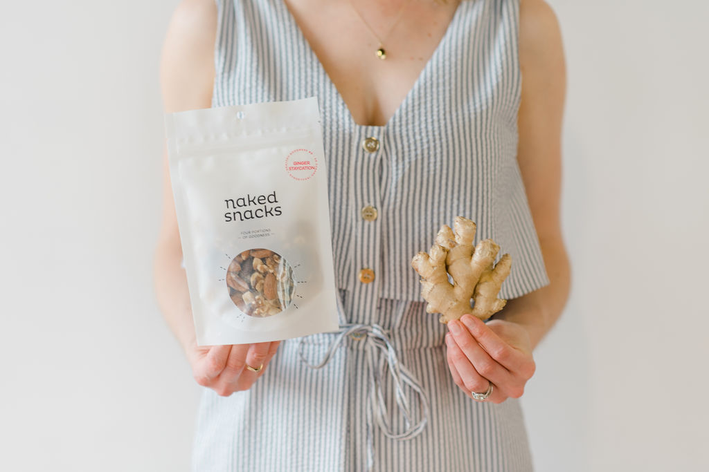 Ginger staycation snack mix from naked snacks, held next to a piece of ginger