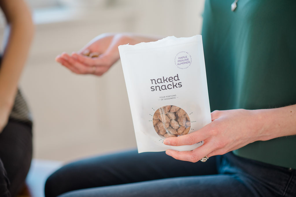 A bag of maple praline almond snacks with a hand holding a fistful in the background
