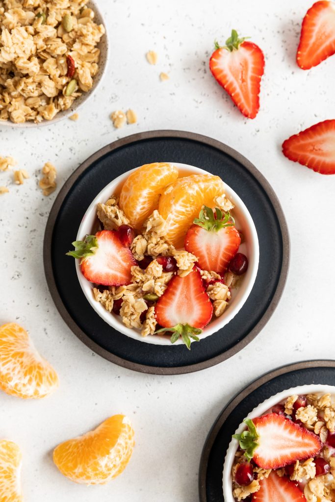 Parfait bowl with granola, oranges and strawberries in a white bowl.